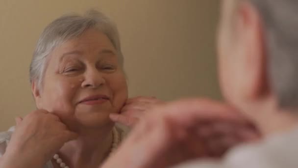 Ritratto di donna anziana felice davanti allo specchio che applica la crema sul viso — Video Stock