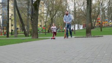 Mutlu baba ve küçük kız parkta scooterla geziyorlar. Aile ve babalık kavramı