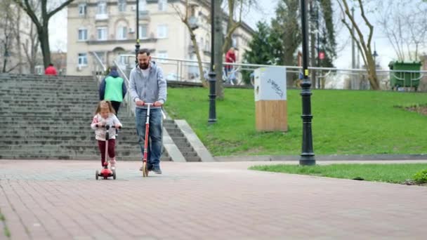 Feliz padre y su hijita montando scooters en el parque. concepto de familia y paternidad — Vídeo de stock