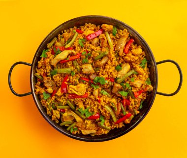 Sarı arka planda tavuklu İspanyol paella pilavı.