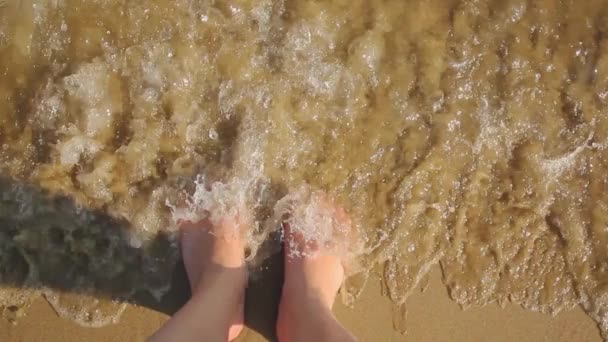 Жіночі ноги стоять на піску пляжу з морською піною, вид зверху — стокове відео