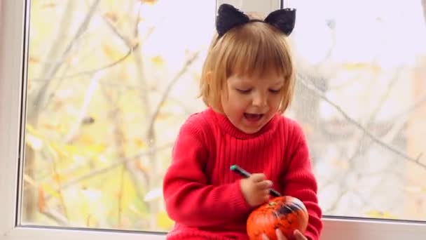 Kleines Mädchen bemalt Kürbis für Halloween und singt zu Hause — Stockvideo