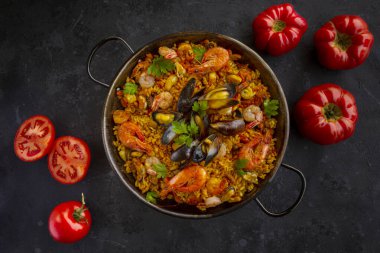 Siyah arka planda domatesli geleneksel İspanyol deniz ürünleri paella 'sı