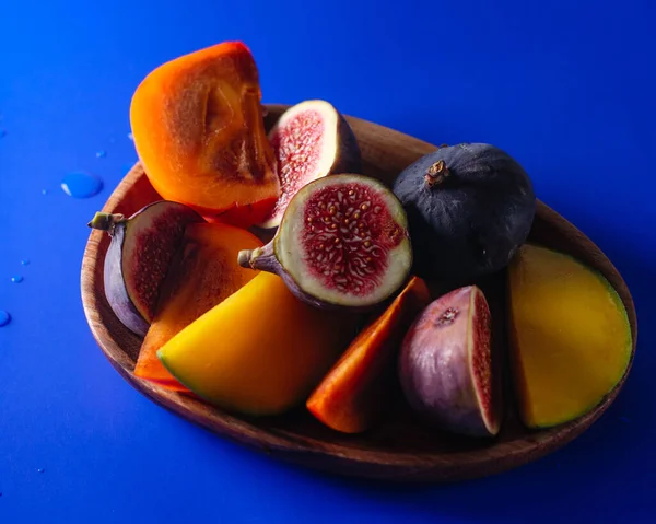 Persimmon, figs and mango sliced on a wood platter top view on blue