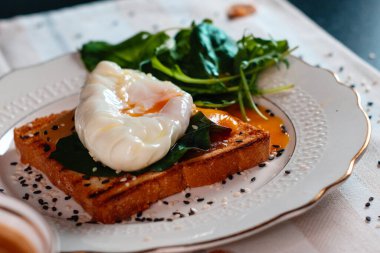 Sağlıklı kahvaltı, haşlanmış yumurta ve yeşil salata yaprakları. Yumurta sarısı yayılmış.