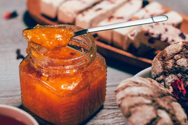 Ahşap masanın üzerinde turuncu reçel kavanozu var. Arkaplanda bulanık çikolatalı bisküvi ve lokum.