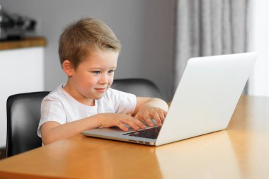 Evde bir masanın üstünde dizüstü bilgisayar kullanan genç bir çocuk.