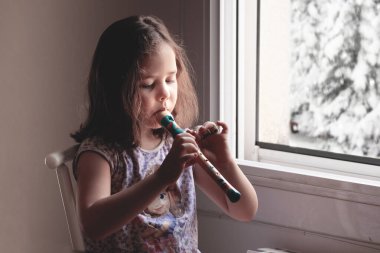 Sarışın, beyaz bir kız evde flüt ağları çalıyor. Düzenleyicinin metni için boş kopyalama alanı.