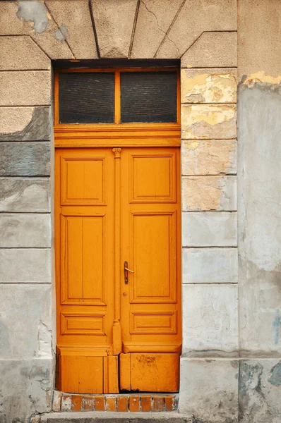 Old wooden front doors. Orange front doors. Dilapidated facade with wooden orange doors.