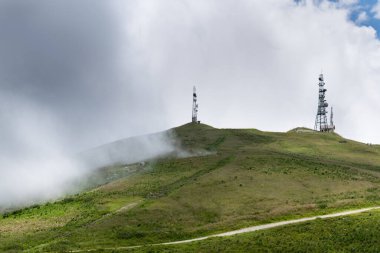 Bulutlu bir günde, yemyeşil çayırlar ve iki anten ile kaplı dağlık bir zirve. Nevegal, Belluno, İtalya