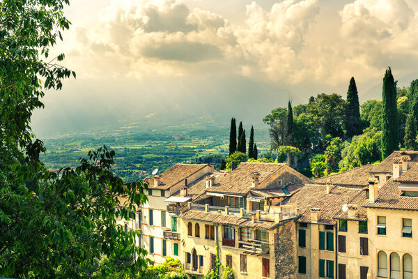 Panorama of the ancient village of Asolo that climbs up the hill dense with lush vegetation in summer. Glimpse of the valley with stormy sky. Treviso, Italy