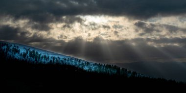 Yüksek zıt karlı dağ manzarası. Güneş ışınları bulutları delip geçiyor. Firavun Ormanı. Alpe del Nevegal, Belluno, İtalya