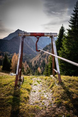Bulutlu gökyüzü, dağlar ve ağaçlarla kaplı yamaçlar. Ön planda bir kablo var. Cesiomaggiore, Belluno, İtalya