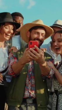 Neşeli bir arkadaş grubu dışarıda keyifle vakit geçiriyorlar, akıllı telefon kullanarak keyifli anları yakalıyorlar.