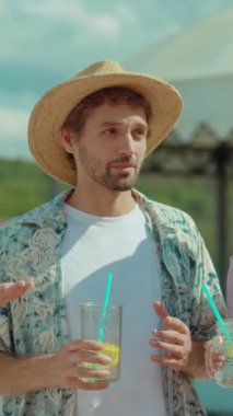 Bir adam güneşli bir açık havada serinletici bir içecekten hoşlanır. Bu da yaz rahatlığının özünü yakalar.