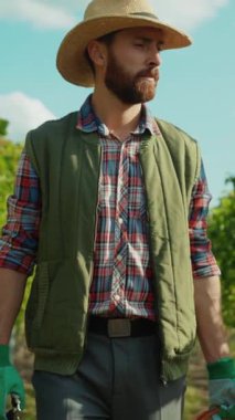 Ekose bir gömlekle birlikte hasır şapka takan bir adam dışarıda duruyor, kırsal bir yaşam tarzını somutlaştırıyor.