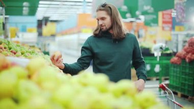 Süpermarketten elma alan yakışıklı bir adam gülümseyen bir meyve meyvesi yetişkin tüketiciyi seçen sağlıklı yaşam tarzı erkek organik ürün mağazası perakende satış portresi yakın plan