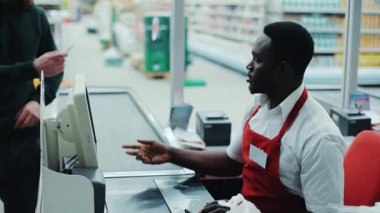 Yazar kasada gülümseyen Afrikalı Amerikalı adam, satış elemanı pazarda perakende satış yapan süpermarketin sağlıklı, sağlıklı, siyah, sağlıklı ve ağır çekimde mal aldığını sayıyor.