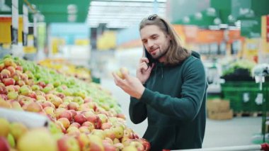 Gülümseyen adam telefondan elma seçer süpermarketten alışveriş teknolojisi müşteriler hakkında konuşur arka plandan konuşur akıllı telefon satın alır gündelik tüketici piyasası yavaş çekim satın alır