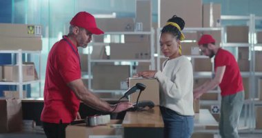 Postanede, günlük giysiler içindeki genç Afro-Amerikalı bir kadın teslimat kutusunun teslimatı için ödeme yapıyor. Teslimat bölümünde çalışan erkek ekip..