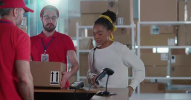 Paket almak için postaneye gelen modern, genç Afrikalı bir kadın. Birkaç genç ve olgun posta işçisi müşterilerine karton kutu teslim ediyor..