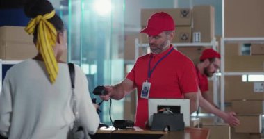 Postane hizmetleri. Genç Afro-Amerikan kadın teslimat departmanı karton kutu paketi almaya geldi. Beyaz tenli kibar işçi müşterilere hizmet ediyor..