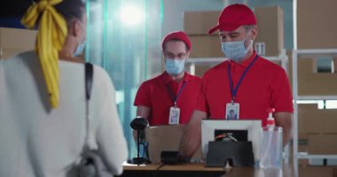 Karantina konsepti. Postane müşterileri ve personel iletişim için tıbbi maske takıyor. Çevrimiçi sipariş için ödeme yapan Afrikalı genç bir kadın teslimat kutusu alıyor.