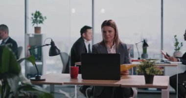 Genç sarışın, yetişkin, beyaz kadın ofis yöneticisi şirket görevlerini portatif dizüstü bilgisayarda yürütüyor..