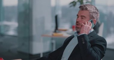 Kafkasyalı yetişkin işadamı, ofis iş merkezinde çalışırken haberleşmeyi paylaşan aşınmış bir partnerle cep telefonuyla konuşuyor..