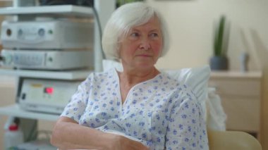 Yaşlı, mutlu, beyaz kadın büyükanne hastane yatağında yatıyor. Hastalık iyileşiyor. Ailesinden kameraya gülümseyen destek alıyor. Sağlık ve insanlar konsepti.
