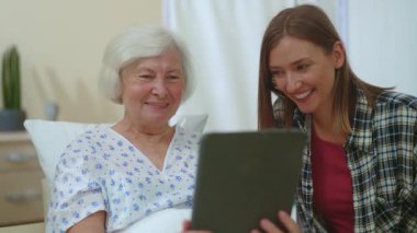 Beyaz tenli güzel kadınlar, yaşlı anne ve küçük kızı, akrabalarıyla birlikte kapalı alandaki hastane odalarını gösteren video sohbet tabletleri kullanıyorlar. Hastalar. Aile desteği. Çevrimiçi ilişkiler.