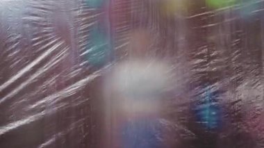 Plastik film bariyerini aşan bir kadın, yapışkan filmin arkasında bulanık bir siluet.