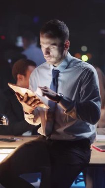 Genç bir profesyonel, gece geç saatlere kadar şık bir ofiste çalışarak bir tablete özenle odaklanıyor.