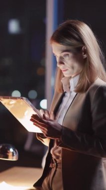 Odaklanmış bir kadın, gece çağdaş bir ofiste, kendini adamışlık ve teknolojiyi gösteren bir tablet kullanır..