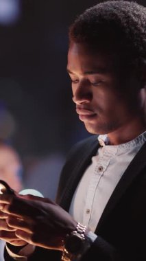 Odaklanmış bir birey, şık bir kıyafet giyerken ekranı tarafından parlak bir şekilde aydınlatılan akıllı telefonunu kullanıyor.