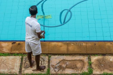 Görevli bir elektrikli süpürge ile havuzu alt temizler.