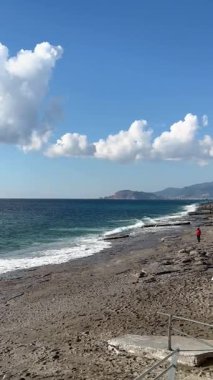 Sakin bir sahil sahnesi sergilendi. Huzurlu bir sahil sahnesi. Sahilde bulutların altında yalnız bir kişi, sakin bir sahil manzarası.