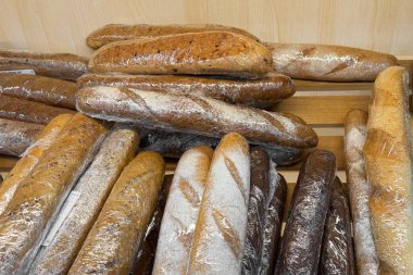 Tepside istiflenmiş taze ekmek, altın kabukları ve un tozu, düzenli olarak üst üste binen uzun somunlar, satışa hazır fırın rafı, sıcak sabah ışığı, davetkar aroma önerisi,