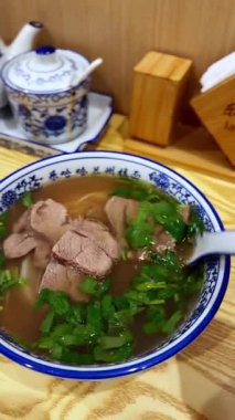 Asya usulü erişteli erişte çorbası taze otlarla servis edilir, ahşap bir masada mavi-beyaz porselen kasede servis edilir..