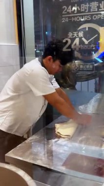 Aşçı, restoranın mutfağındaki metal bir masada hamurdan taze erişte çıkartıyor. Geleneksel erişte yapma süreci, sokak yemeği tarzı, camların arkasındaki gece sahnesi..