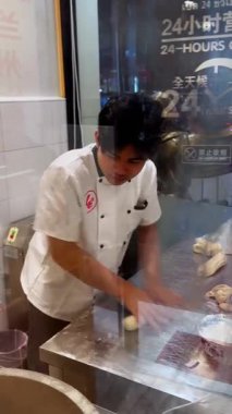 Aşçı, restoranın mutfağındaki metal bir masada hamurdan taze erişte çıkartıyor. Geleneksel erişte yapma süreci, sokak yemeği tarzı, camların arkasındaki gece sahnesi..