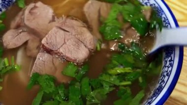 Asya usulü erişteli erişte çorbası taze otlarla servis edilir, ahşap bir masada mavi-beyaz porselen kasede servis edilir..