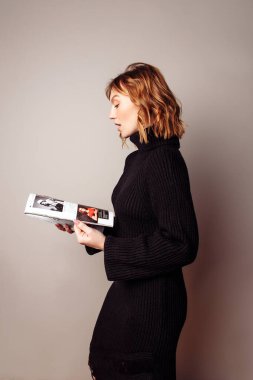 Güzel bayan bir dergiye bakıyor, siyah örülü elbise giyiyor. Dalgalı sörf saç stili. 