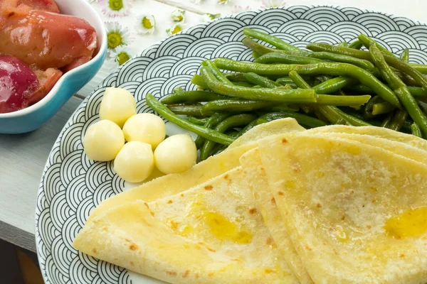 Traditional food from Slovakia. Salty pancake from potato flour dough. Smeared with melted butter. Served with green bean pods, cheese and caramelized sweet apples.