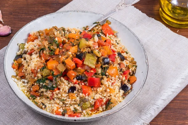 couscous with stews is a Moroccan and Tunisian dish. Couscous mixed with stewed vegetables in a large bowl on a linen napkin on a wooden table, top view