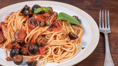 Spagetti alla vesuviana, soslu ve domatesli makarna, zeytin, soğan ve kapari kırsal bir ahşap masada bir tabakta - İtalyan yemeği