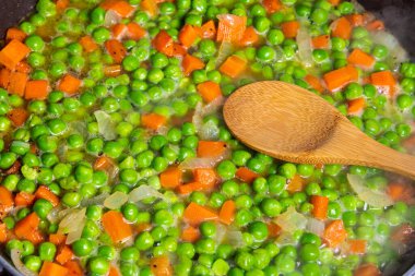 Bezelye ve havuçla makarna pişirmek. Kızartma tavasında bezelye, havuç ve soğan pişirmek..