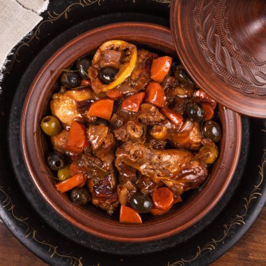 Tahta bir masa üzerinde baharatlı soslu zeytin ve sebzeli Cezayir güvecinde tavuk hazır olsun.