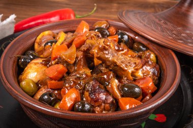 Tahta bir masa üzerinde baharatlı soslu zeytin ve sebzeli Cezayir güvecinde tavuk hazır olsun.