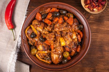 Tahta bir masa üzerinde baharatlı soslu zeytin ve sebzeli Cezayir güvecinde tavuk hazır olsun.